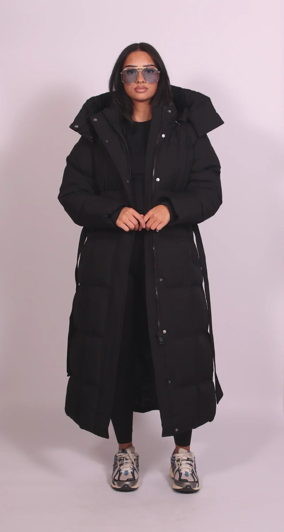 Model in a black puffer coat with buttons, hood, and zipper, standing in a studio with a plain backdrop.
