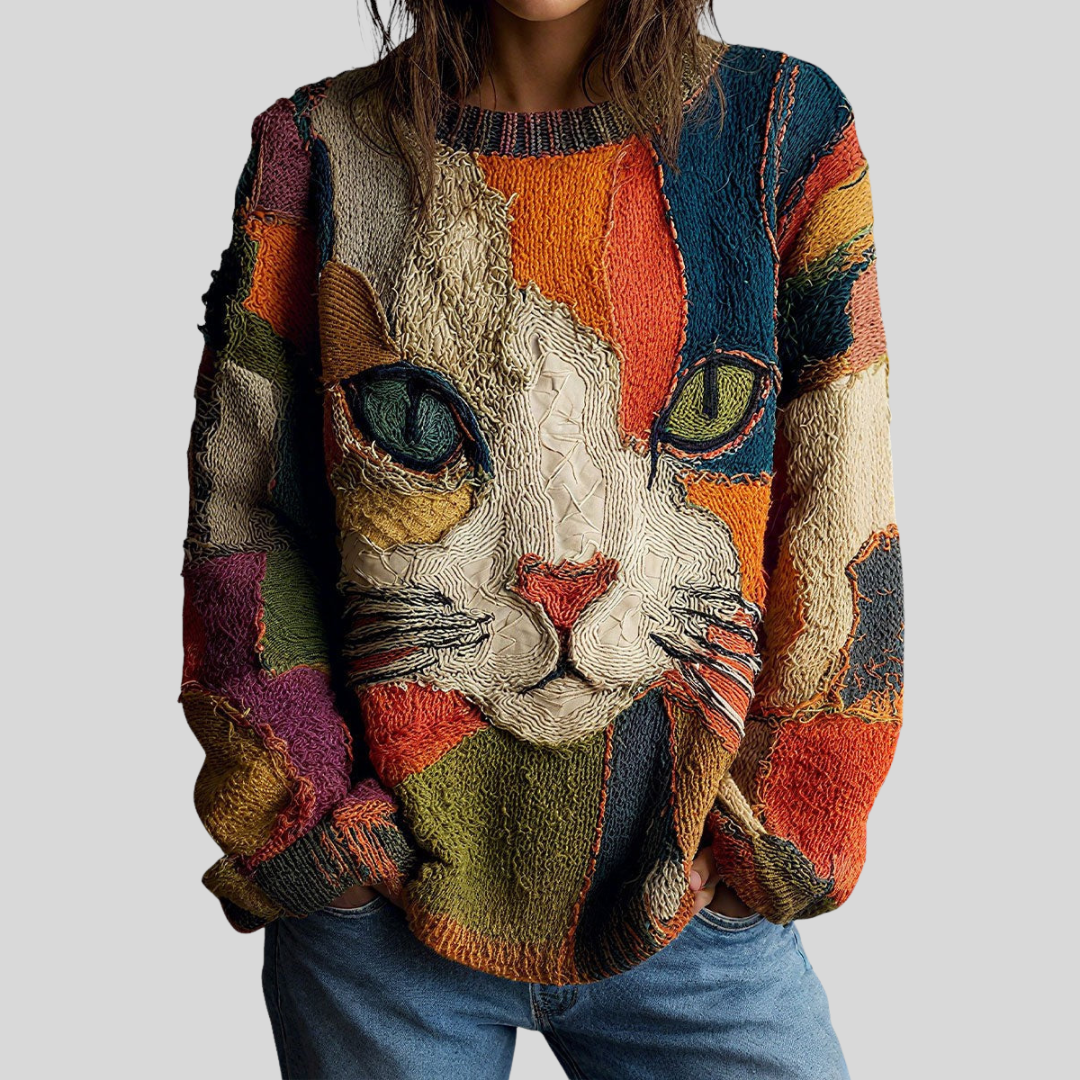 Person wearing a textured top featuring a colorful artistic cat face design, set against a plain gray background.