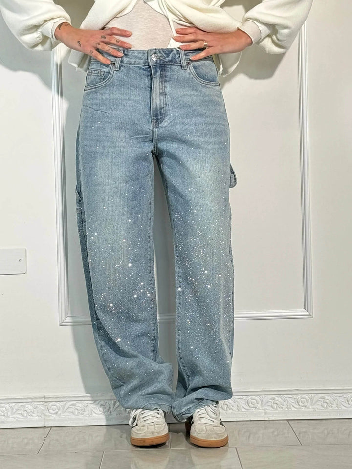 Model in light blue diamond-detailed trousers with white wrap top and sneakers in an airy studio setting.