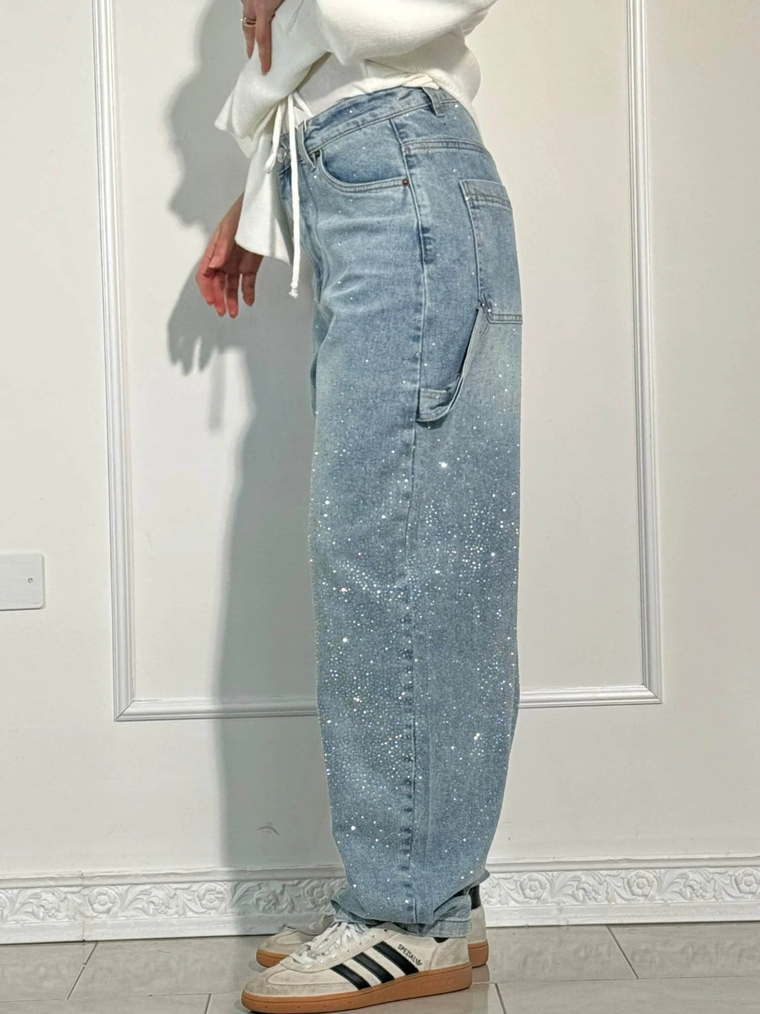 Side view of light blue diamond-studded trousers with striped sneakers, shown in a light studio.