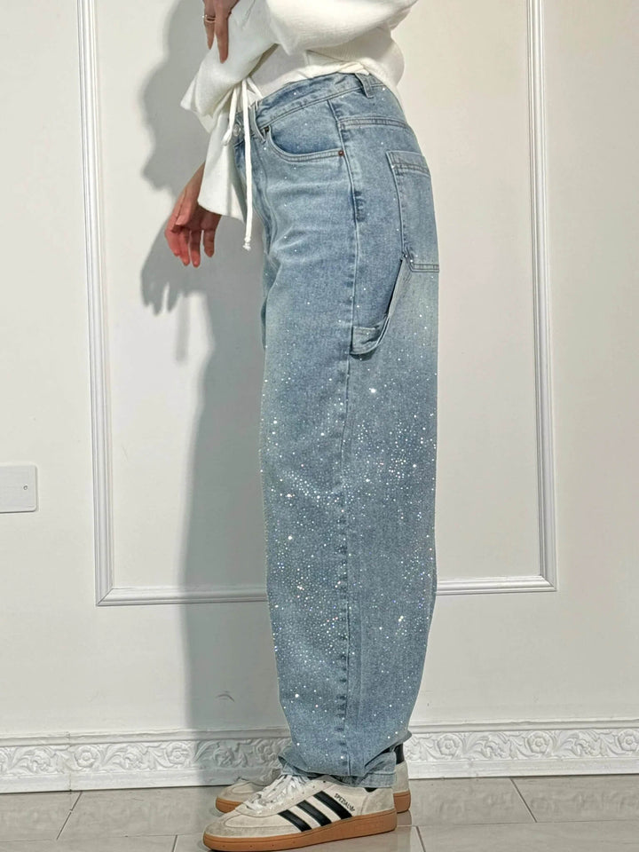 Side view of light blue diamond-studded trousers with striped sneakers, shown in a light studio.