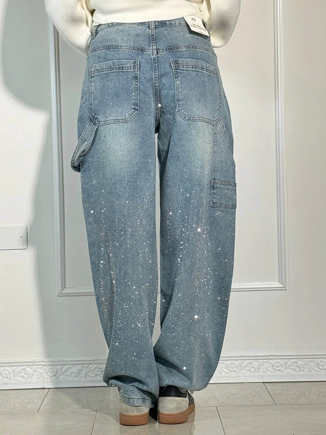 Back view of light blue sparkling trousers with large pockets, paired with white sneakers in a bright studio.