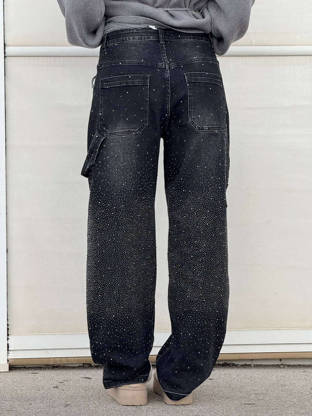 Back view of black sparkling trousers paired with fur-lined slippers in an outdoor environment.