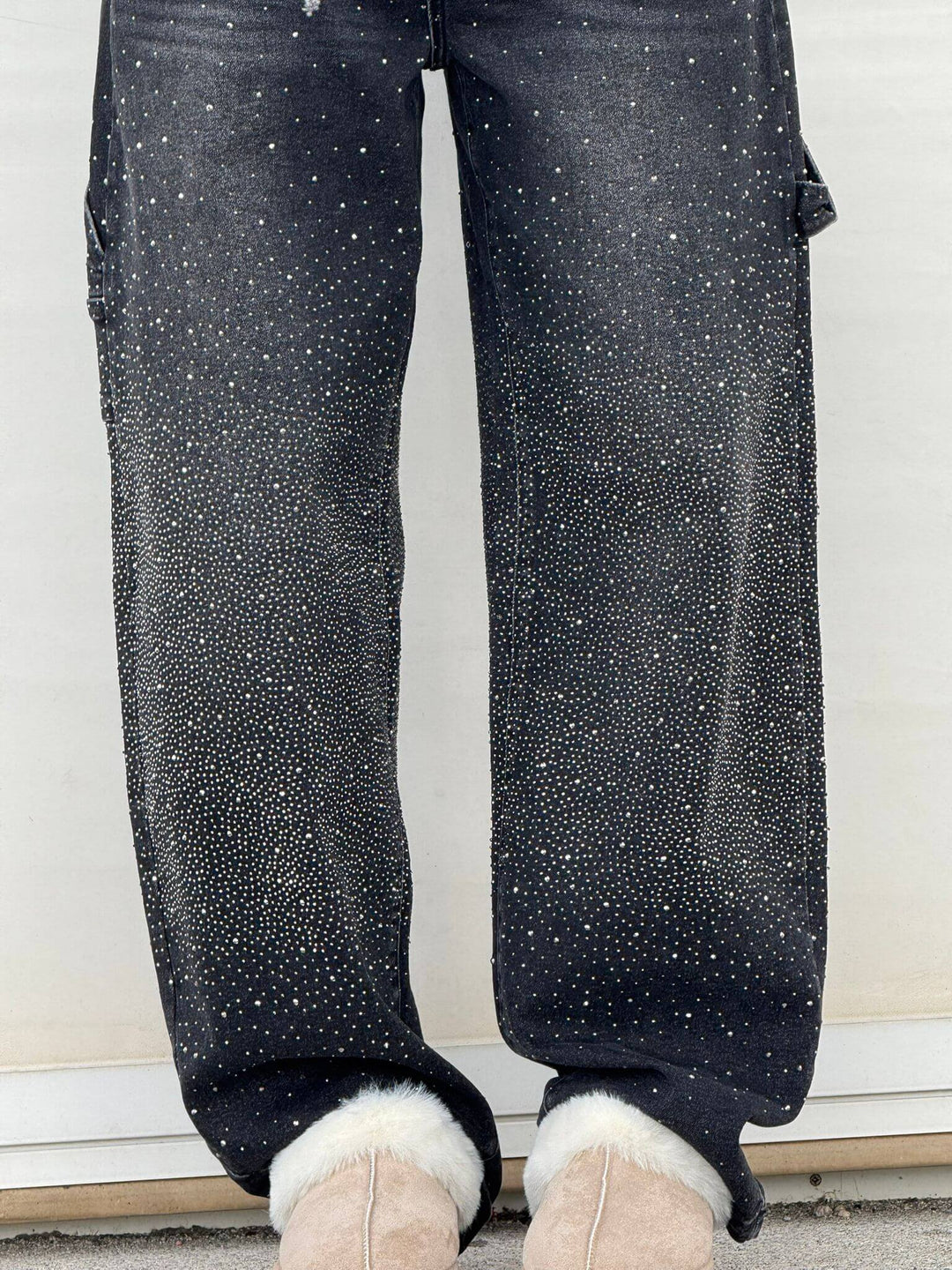 Close-up of black diamond-embellished trousers with fur slippers in an outdoor scene.