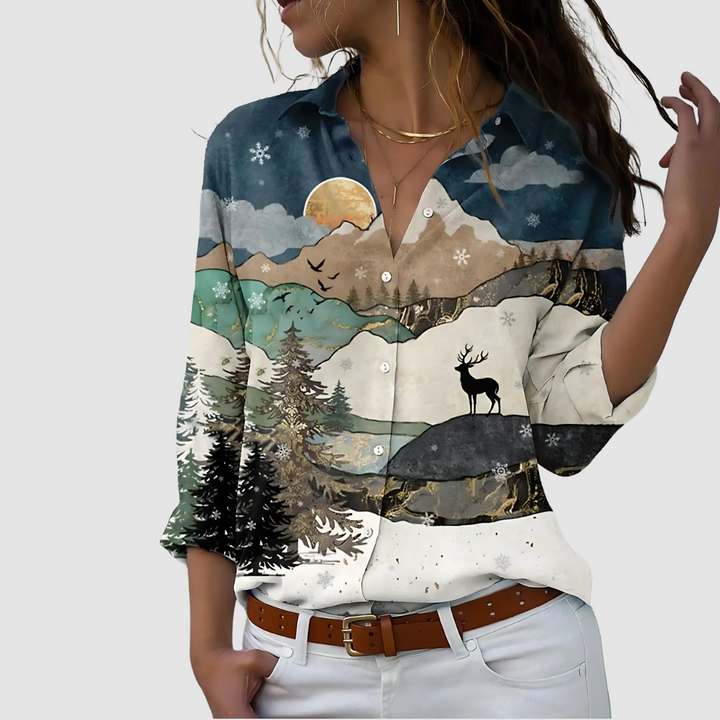 Soft blouse depicting a scenic mountain and deer landscape, styled with white pants against a plain backdrop.