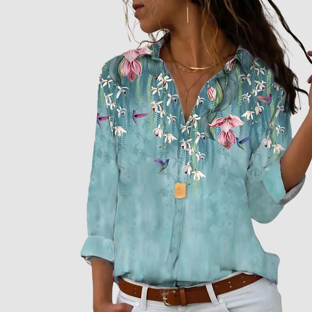 Soft blouse in aqua with floral and hummingbird designs, styled with white pants against a neutral background.