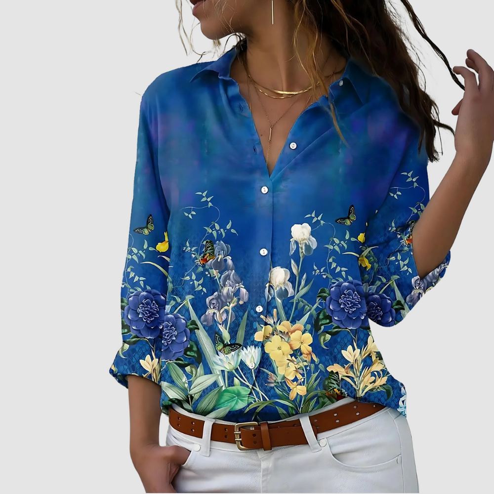 Soft blouse featuring a vibrant blue background with floral and butterfly motifs, styled with white pants in a studio.