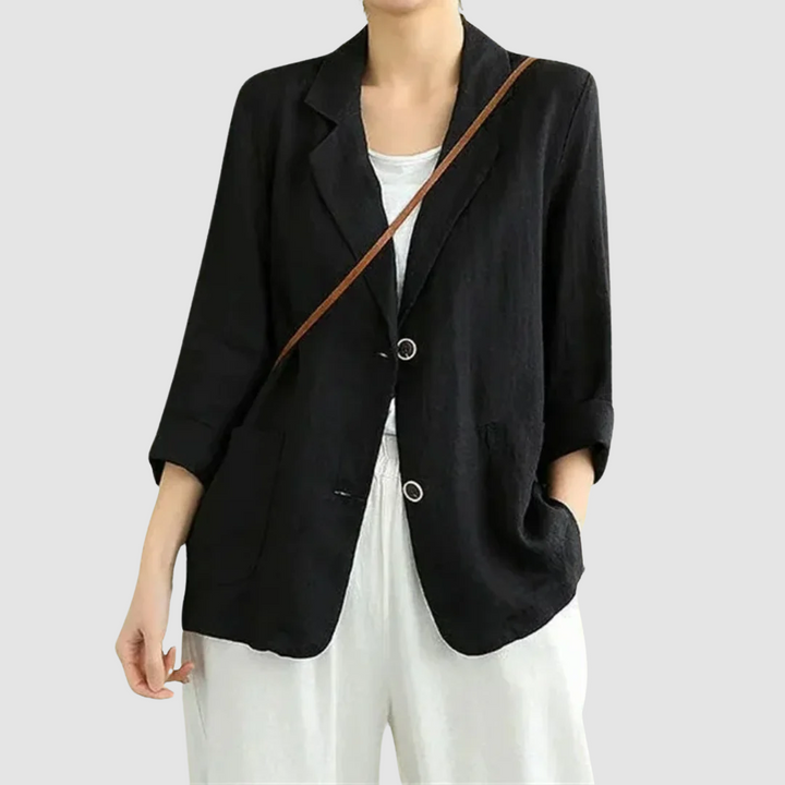 Casual chic black blazer with rolled sleeves and front pockets, styled over a white top and shorts, set against a light gray background.