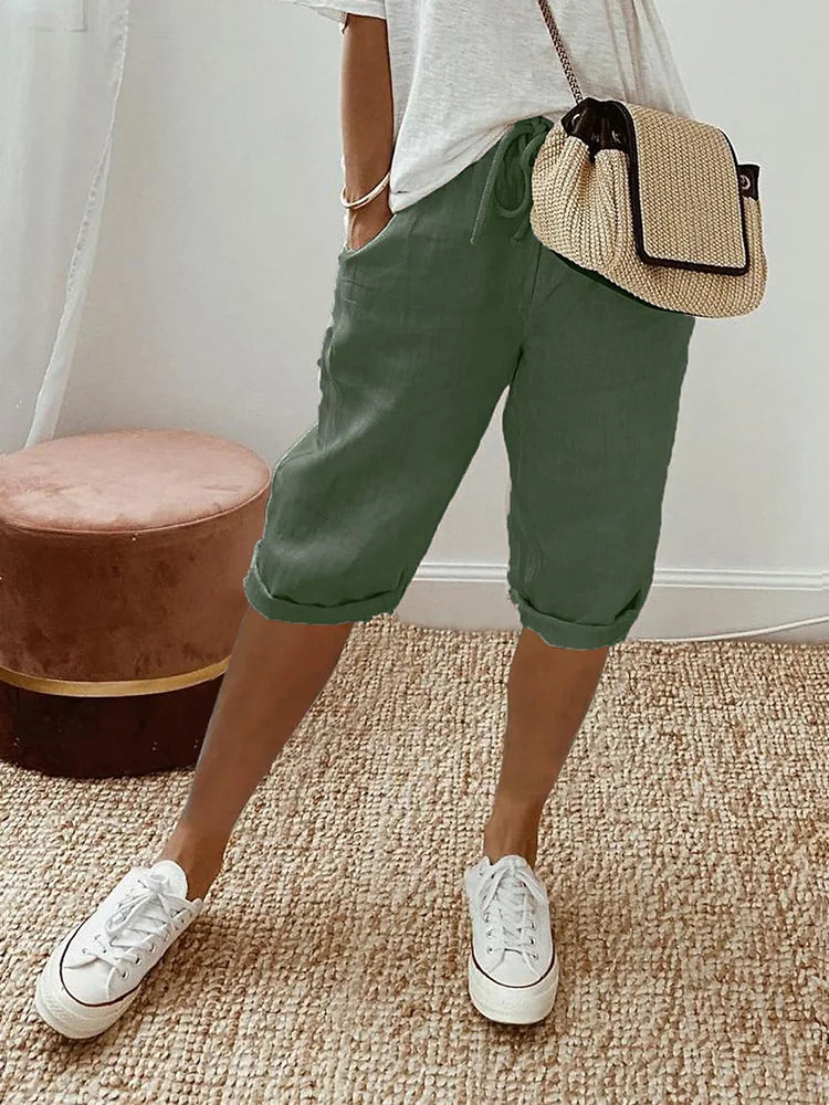 Green comfort shorts styled with a white top and sneakers, displayed in a cozy indoor space with woven rug and stool.
