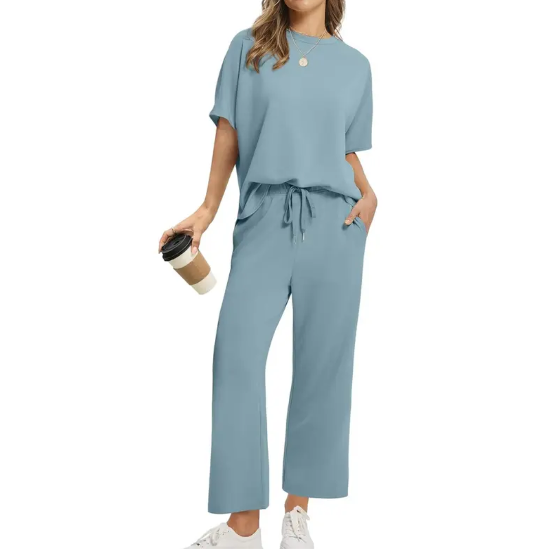 Woman modeling a chic light blue set with loose top and drawstring pants, holding a coffee, studio atmosphere.