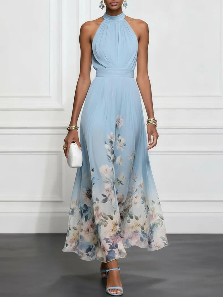 Elegant blue maxi dress with floral hem, halter neck, and accessories, in a white-walled studio.
