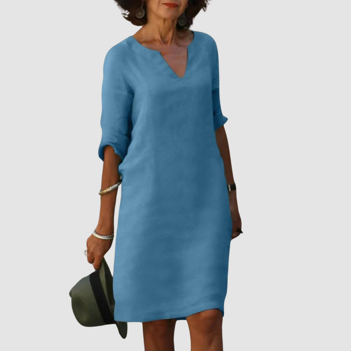 Elegant light blue V-neck dress with mid-length sleeves, modeled with hat and jewelry on neutral background.