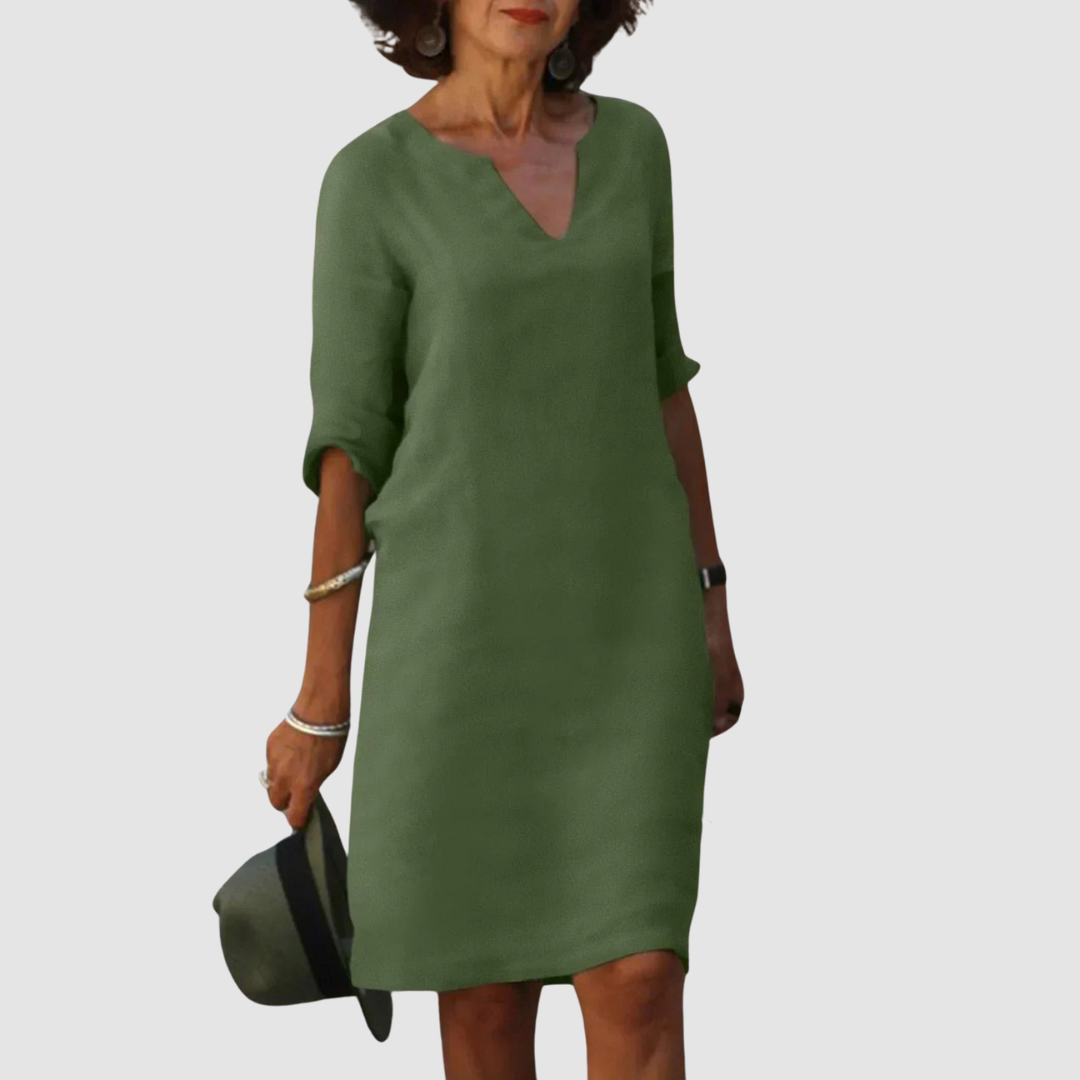 Elegant green V-neck dress with mid-length sleeves, modeled with hat and jewelry on neutral background.