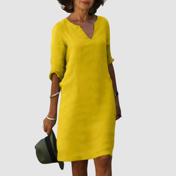 Elegant yellow V-neck dress with mid-length sleeves, modeled with hat and jewelry on neutral background.