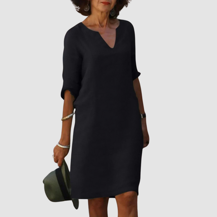 Elegant black V-neck dress with mid-length sleeves, modeled with hat and jewelry on neutral background.