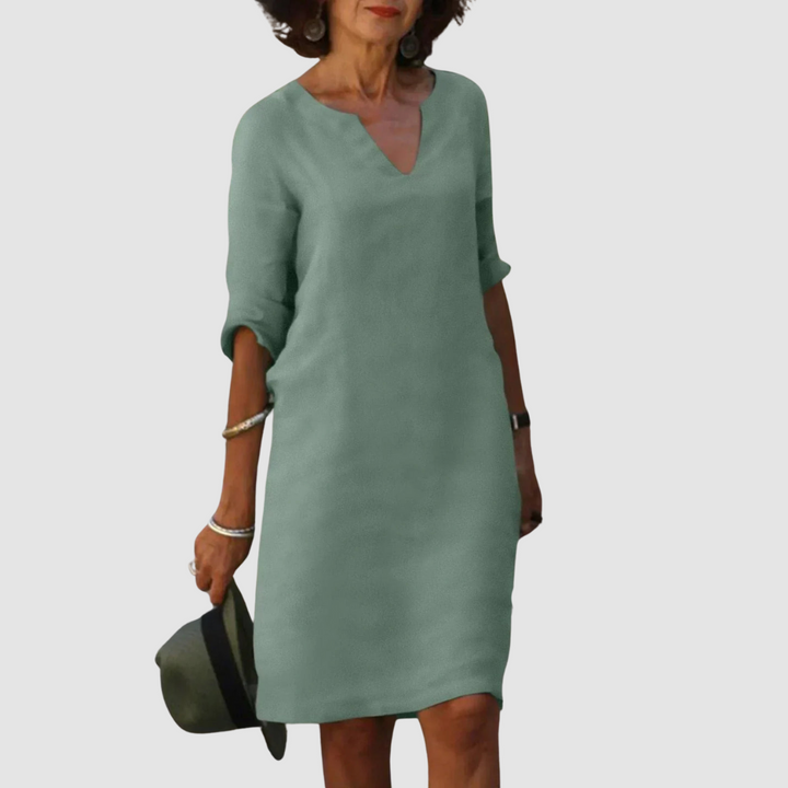 Elegant light green V-neck dress with mid-length sleeves, modeled with hat and jewelry on neutral background.