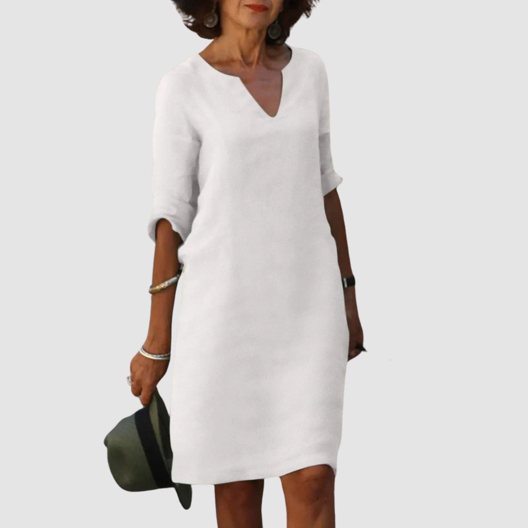 Elegant white V-neck dress with mid-length sleeves, modeled with hat and jewelry on neutral background.