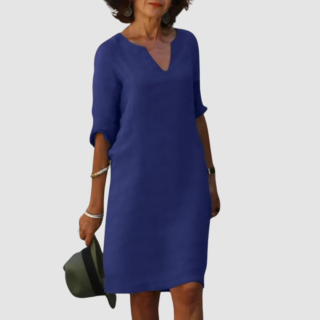 Elegant dark blue V-neck dress with mid-length sleeves, modeled with hat and jewelry on neutral background.