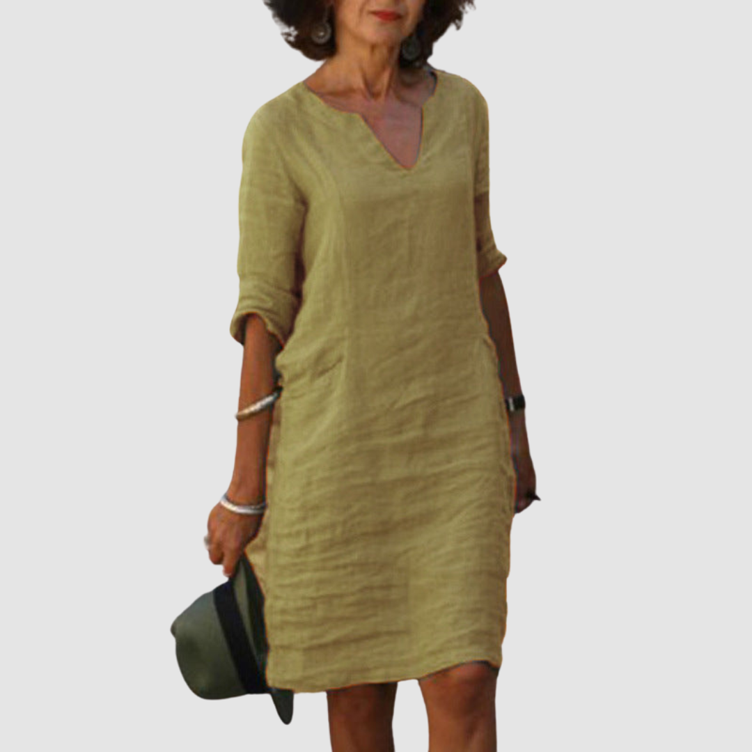Elegant beige V-neck dress with mid-length sleeves, modeled with hat and jewelry on neutral background.