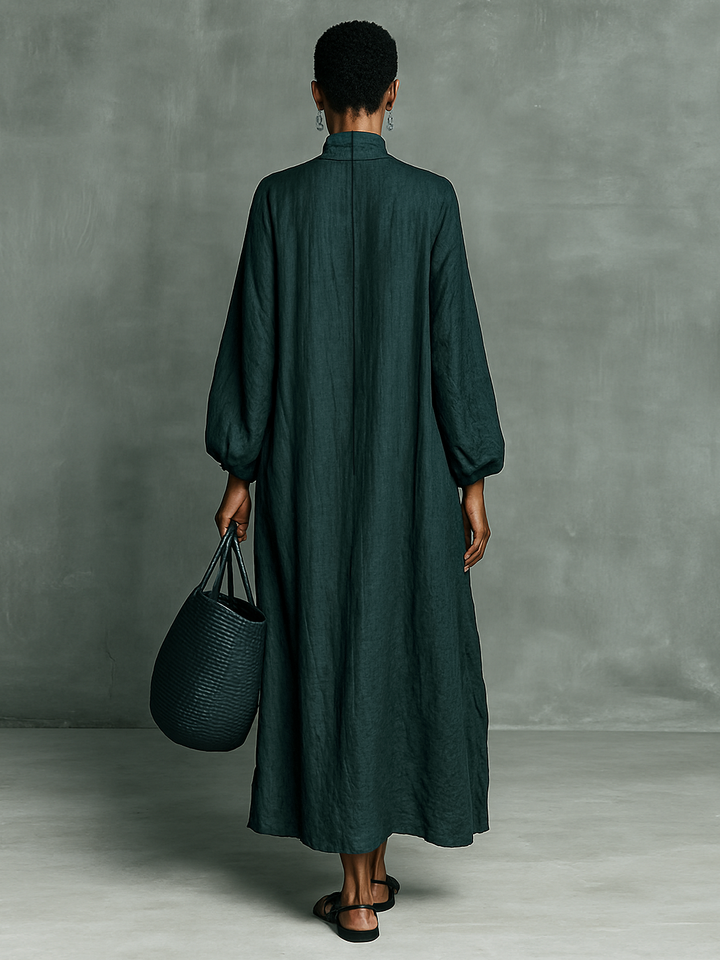 Back view of model in green maxi dress holding a woven tote against a minimal studio background.
