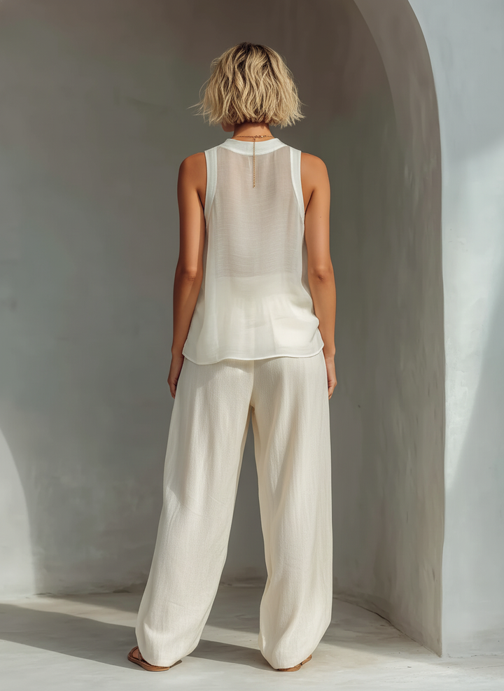 Back view of model wearing elegant white outfit, showing flowy top and pants in serene environment.