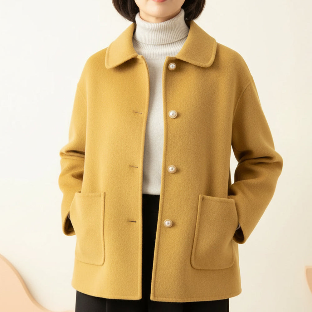Yellow jacket worn over white turtleneck, hands in pockets, in a neutral room.