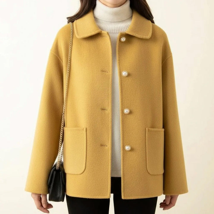 Yellow jacket worn with white turtleneck, holding black purse, in a neutral space.