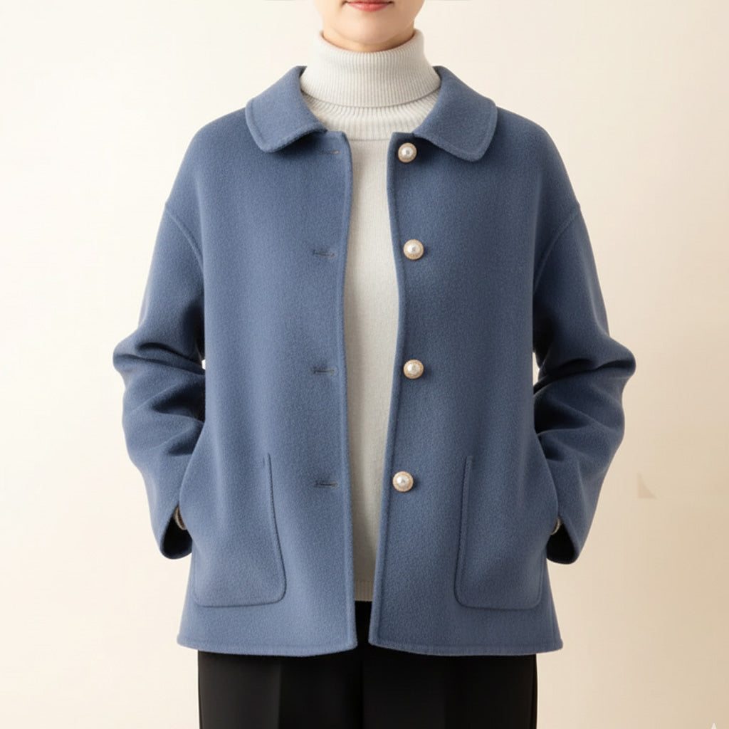 Blue jacket worn over white turtleneck, hands in pockets, in a neutral room.