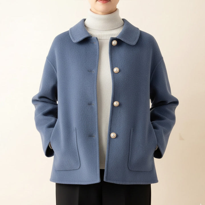 Blue jacket worn over white turtleneck, hands in pockets, in a neutral room.