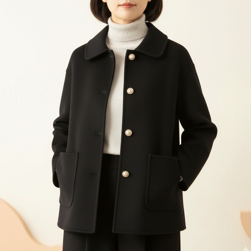 Black jacket worn over white turtleneck, hands in pockets, in a neutral room.