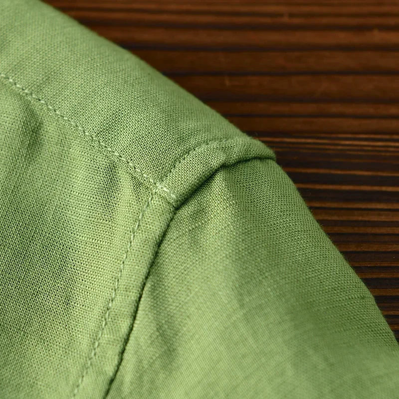 Detail of green linen shirt shoulder stitching on wooden surface.