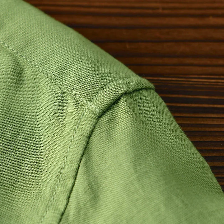 Detail of green linen shirt shoulder stitching on wooden surface.