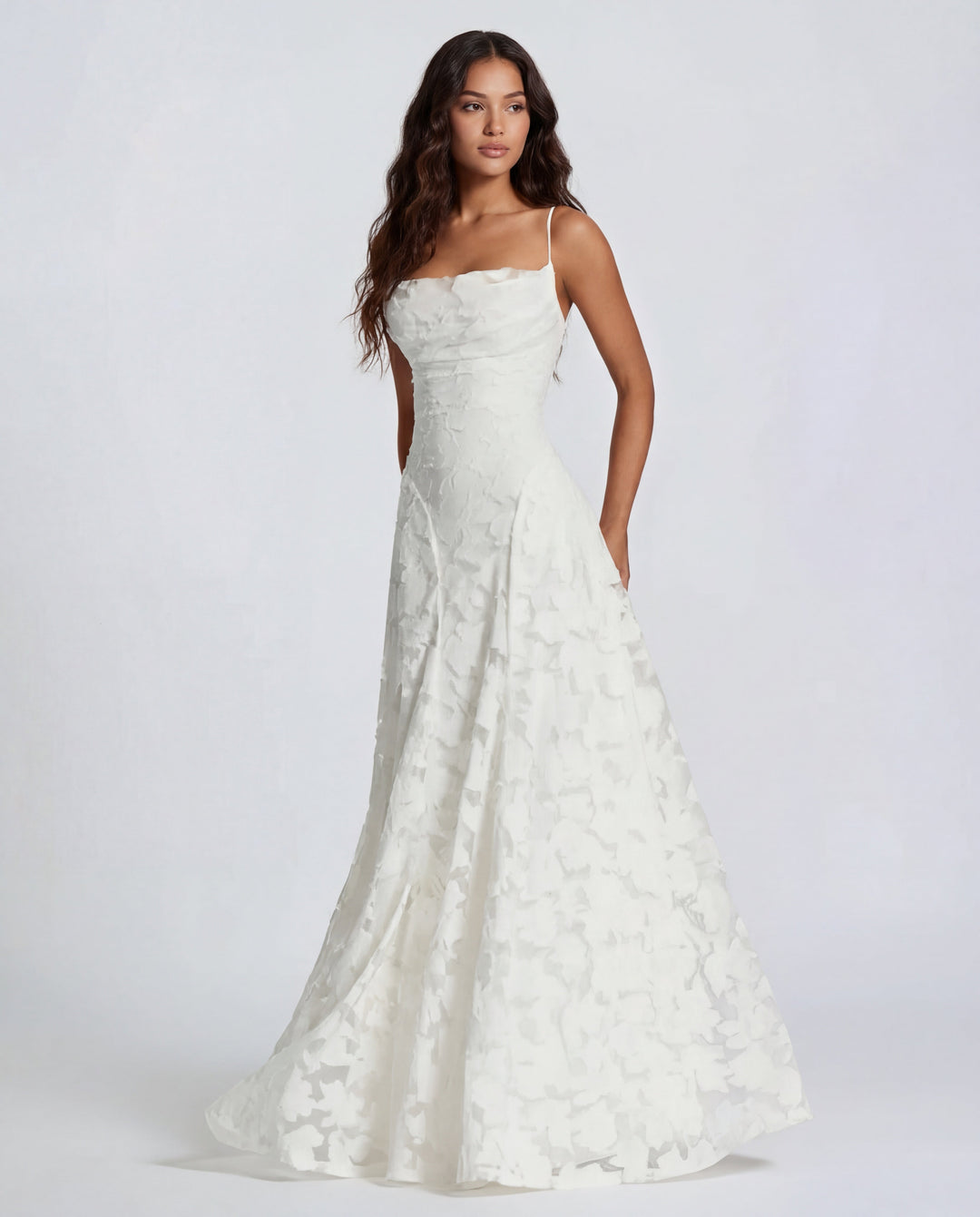 Model in a white maxi dress with thin straps and floral design, studio background.