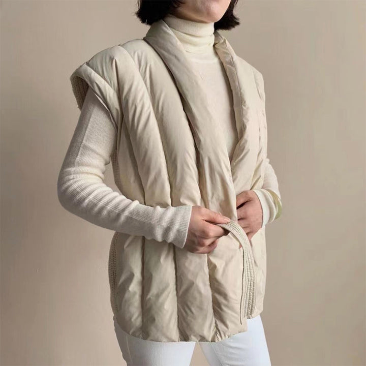 Side view of a cream puffer vest with soft belt, over a turtleneck. Studio background.