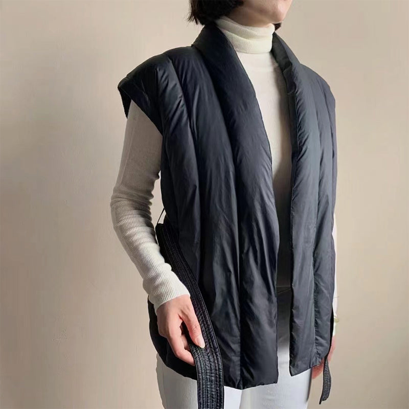 Side view of black puffer vest with open soft wrap, over a turtleneck. Studio background.