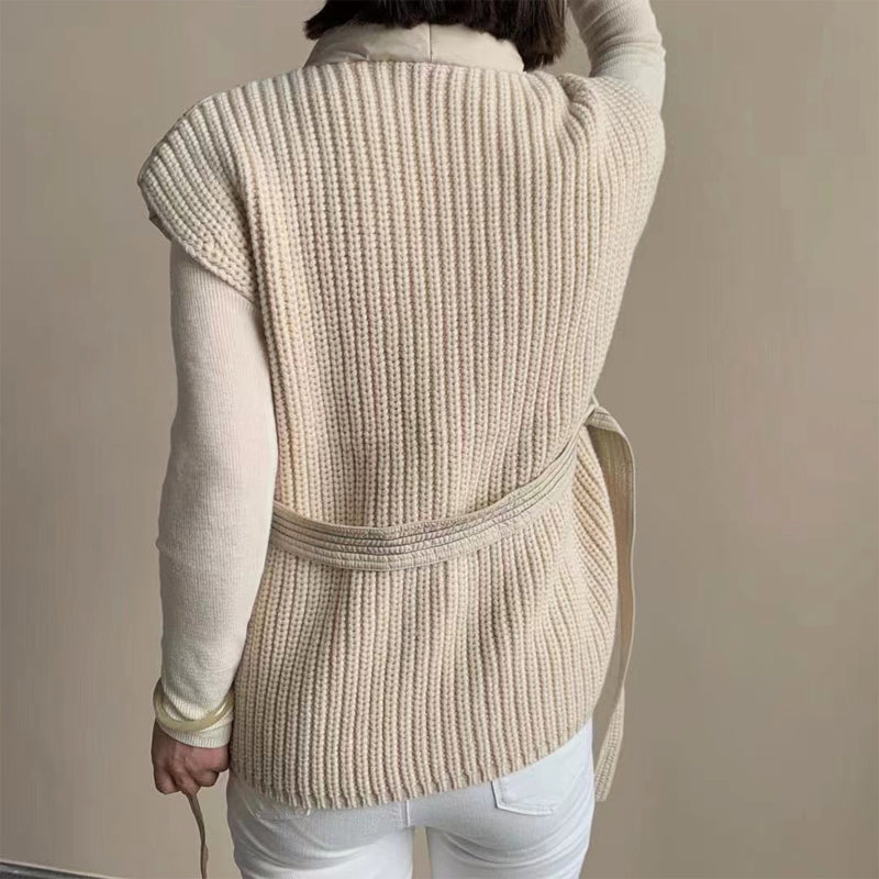 Back view of ribbed cream puffer vest tied at the waist, over a turtleneck. Studio setting.