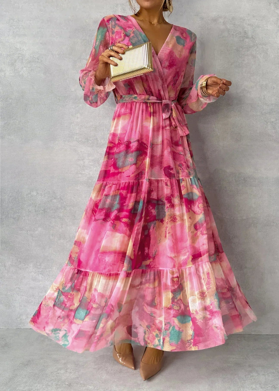 Vibrant floral dress with pink, teal, and gold hues worn in a studio, paired with nude heels and a gold clutch.