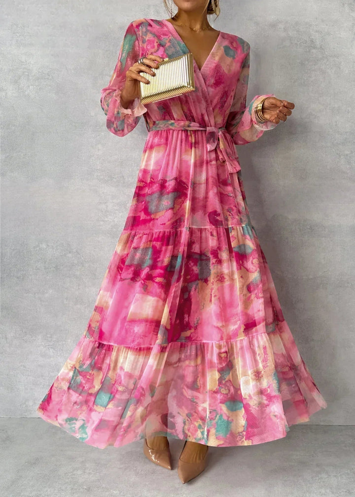 Vibrant floral dress with pink, teal, and gold hues worn in a studio, paired with nude heels and a gold clutch.