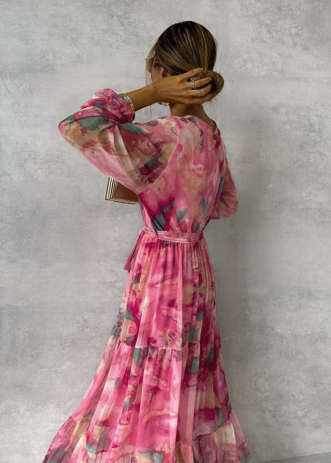 Back view of floral dress in pink, teal, and gold hues in a studio, highlighting flowing texture and tied waist.