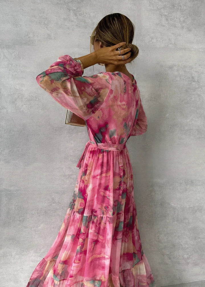 Back view of floral dress in pink, teal, and gold hues in a studio, highlighting flowing texture and tied waist.