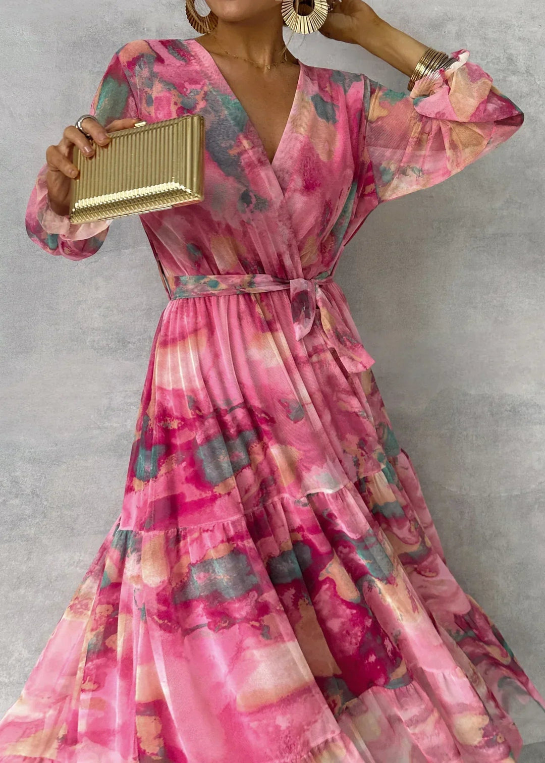 Close-up of floral dress in pink, teal, and gold hues with bold earrings and a gold clutch, set in a studio.