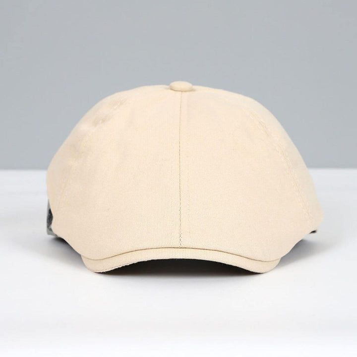 Front view of beige flat cap with a sleek, soft design on a grey and white backdrop.