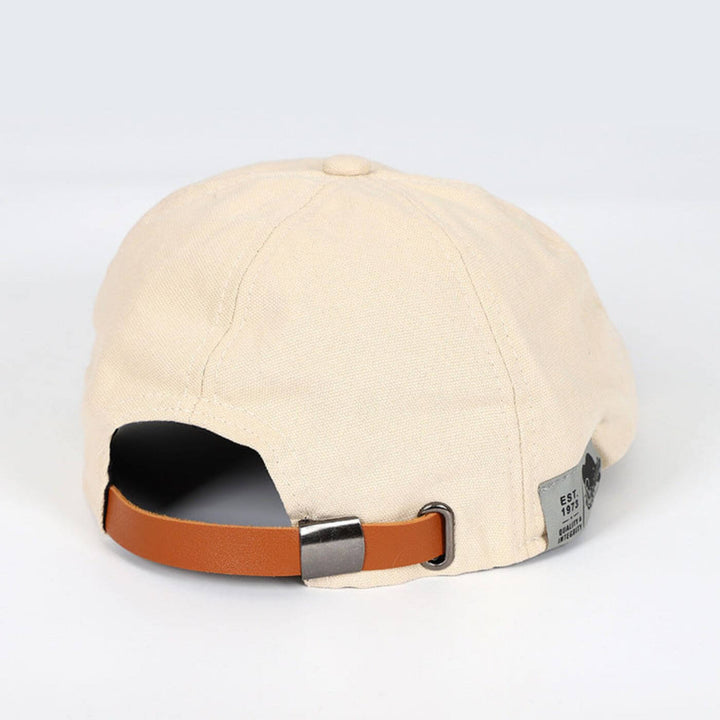 Back view of beige flat cap showing brown strap and tag, set in a minimalist environment.
