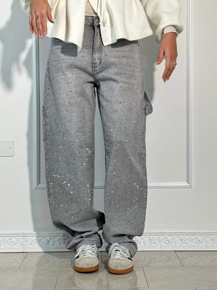 Model wearing gray diamond-studded trousers with white wrap top and sneakers in a bright studio.