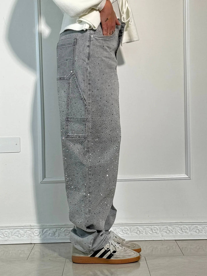 Side view of gray sparkling trousers paired with striped sneakers in a well-lit studio.