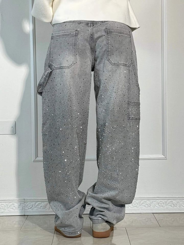 Back view of gray glittering trousers with oversized pockets and sneakers in a bright studio.