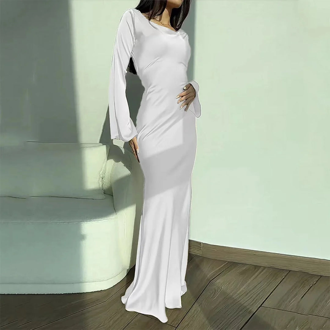 White elegant maxi dress with long sleeves, shown in a sunlit room with wooden flooring and a soft couch.
