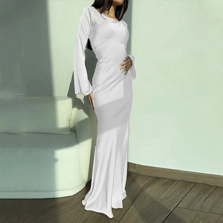 White elegant maxi dress with long sleeves, shown in a sunlit room with wooden flooring and a soft couch.