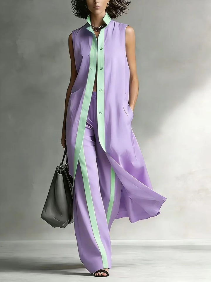 Woman wearing a lavender sleeveless coat and pants set with mint green trim, holding a gray bag in a studio setting.