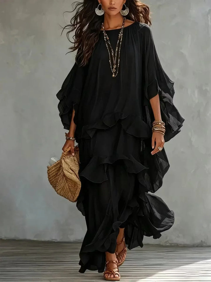 Elegant, layered black dress with flowing ruffles, accessorized with jewelry and a straw bag in a studio.